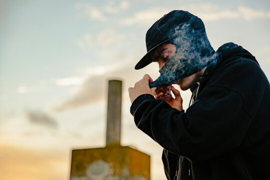 Guy with balaclava smoking a joint of marijuana outdoors