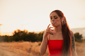 Tattooed girl in a red dress smoking a marijuana joint during sunset