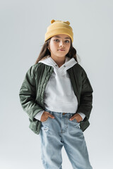 portrait of cute kid in yellow beanie hat and stylish autumnal outfit posing with hands in pockets...