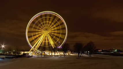 Illuminated ferris wheel at night on a cold winter day with snow on the ground in the Old Port of Montreal, Quebec, Canada. Long exposure with motion blur
