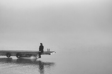 Young woman sitting on the river dock in winter mist