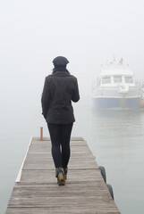 Young woman standing on the river dock in winter mist