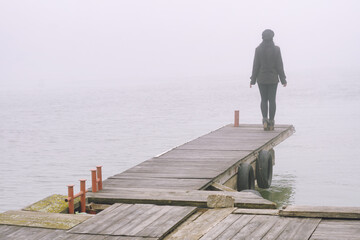 Young woman standing on the river dock in winter mist