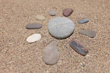 Fototapeta na wymiar Figure of sun is made of pebble stones on sandy beach in summer
