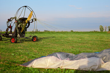 Modern motorized paraglider on a green grass platform in a field is ready to take off into the sky....
