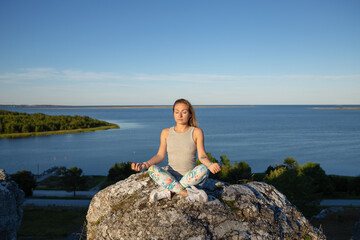 Blondie woman in lotus yoga pose are sitting on the rock near sea cost - 529251814