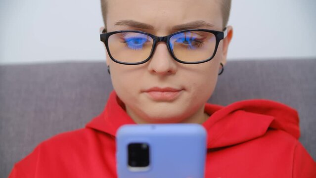 Young short haired woman in glasses browsing smartphone. Focused white female person using modern mobile phone