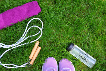 Lavenda color sport shoes ,white jumping rope, purple towel , bottle with fresh water on green grass background. sport for healthy life concept. top view ,free copy space