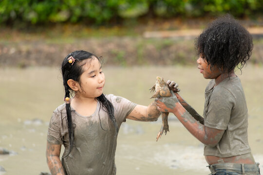 Children have fun playing in the mud in the community fields and catching a frog in a muddy field.