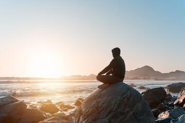 silhouette of a person sitting meditating on the rock on the coast at sunset - obrazy, fototapety, plakaty