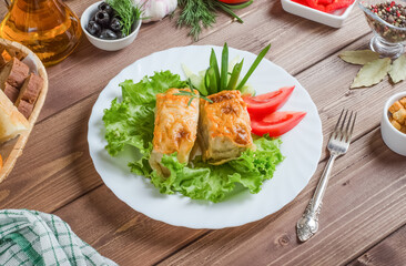 Fried fish fillet pieces with lemon and herbs on a white plate on a dark wooden background