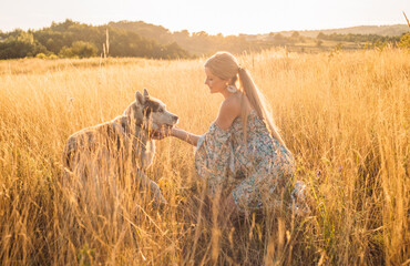 young blonde pregnant female playing with husky dog in the field during sunset in countryside