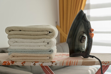 A pile of towels and an iron on the ironing board.