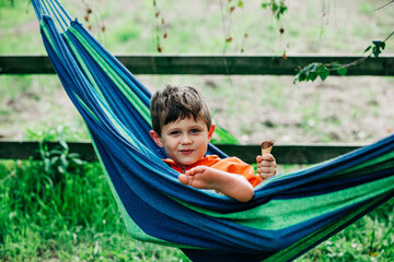 Fototapeta na wymiar Little boy with ice-cream in hammock in village outdoor