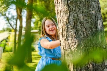 portrait of trisomy 21 child girl outside close to a tree having fun on a park