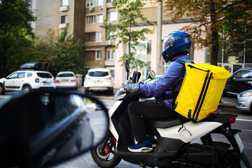 Couriers carry out orders for the delivery of goods on city street. A courier on a motor scooter delivers food.