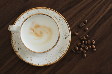 Сup of cappuccino with coffee beans on a brown wooden table, top view
