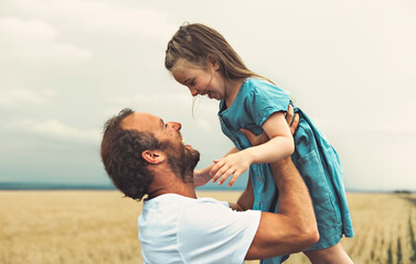 happy child girl and father are playing in wheat field.