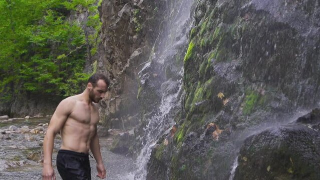 Sporty man wets his hair in front of waterfall.
Muscular sporty young man standing in front of waterfall.

