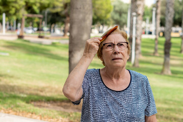 Obraz premium Elderly woman combs her hair in a sunny green park