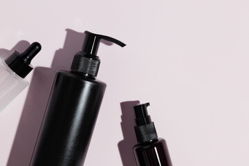 Top view of different black cosmetic bottles on pink background. Mockup.
