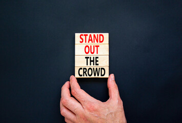 Stand out the crowd symbol. Concept words Stand out the crowd on wooden blocks on beautiful black table black background. Businessman hand. Business, stand out the crowd concept