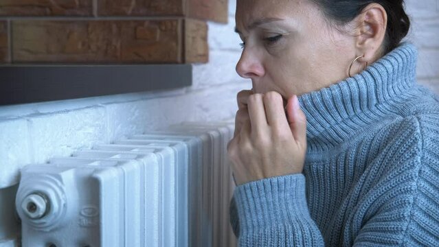 Woman without central heating. A woman in warm pullover get warm by the radiator. A concept of problems with central heating.