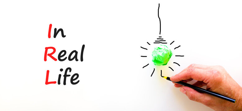 IRL in real life symbol. Concept words IRL in real life on white paper on a beautiful white background. Green light bulb icon. Businessman hand. Business and IRL in real life concept. Copy space.