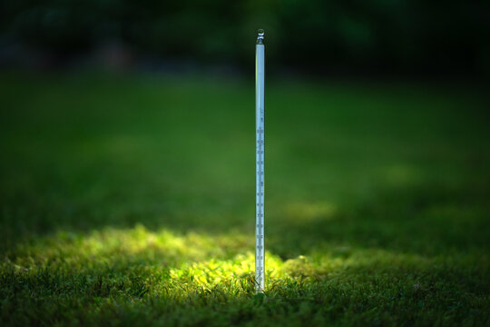A long glass thermometer is stuck in the ground. Measuring the temperature of the earth. The quality of the soil. An increase in the temperature of the earth.