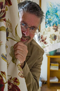 Middle Aged Man Hides Behind A Curtain. With A Playful Smile A Guy Peaks Around The Curtain . 