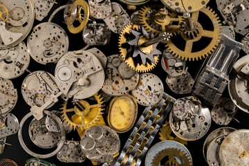 Top view of heap of metal internal parts of old clock. Dial, clockwork, bracelet, gears, cogwheels on black studio background. Disassembled clock mechanism of an old clock. Workshop, repair. Close up.