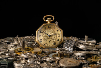 Antique gold pocket watch among clockwork parts on black isolated studio background. Gears,...
