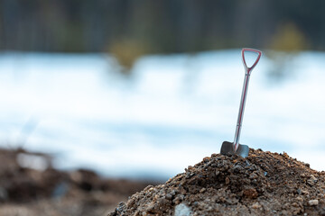 a metal shiny shovel is inserted into a pile of earth. outdoors, the background is blurred