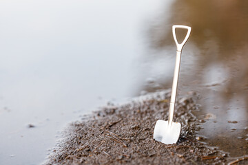 a shovel in the ground on the shore near the reservoir is stuck in the dirty ground
