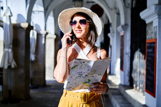 Smiling tourist with paper map talking on cellphone in city