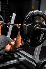 High quality photography. Hispanic man in a black shirt in a gym lying down lifting a heavy weight with both arms. 45 pound weight being lifted.