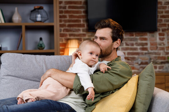 Dad plays with his little baby, on the couch in a cozy apartment. Fatherly love. Father hugs and kisses his little daughter.