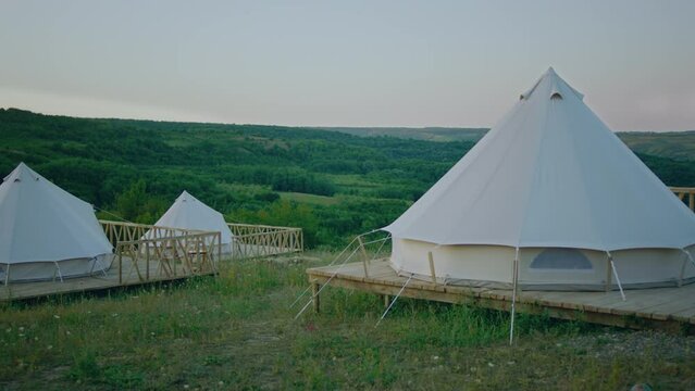 A view of a few teepee style tents outside in the mountains nature in a beautiful atmosphere they are standing in a platform