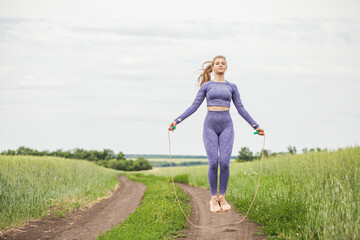 Young blonde woman doing exercises with a skipping rope on a country road