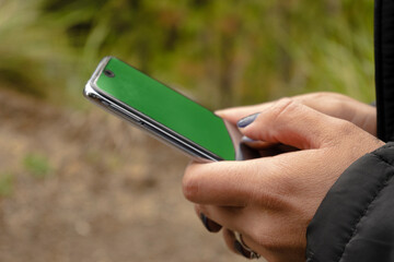 close up woman hands holding a cell phone with green screen in the forest. 5G connection concept
