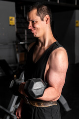 Fototapeta na wymiar High quality photography. Man training in a gym. Caucasian man with a dark background lifting a dumbbell making a lot of effort. Man training arms with dumbbells.