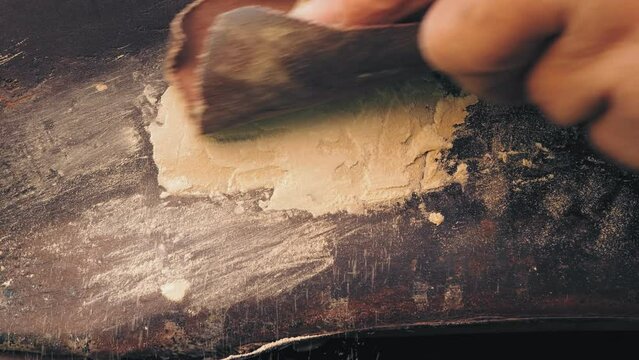 A man's hand rubs excess putty on a car wing with sandpaper. Medium plan