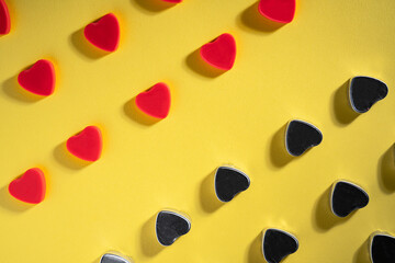 Pattern of rows of red and dark gray hearts on isolated yellow studio background. Crystals, glisten confetti, spangles in form of hearts with reflective shadow. Symbol of love, Valentine's Day.