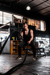 High quality photography. A man in a gym training with ropes. Athlete man on a dark background full of training machines.