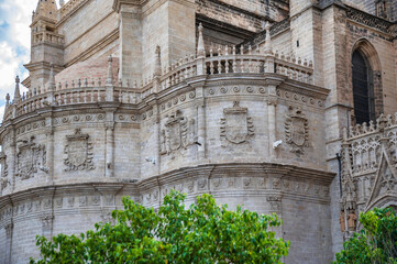 Obraz premium Detailed view of Seville Cathedral’s ornate stone facade with gothic architecture and heraldic shields, Andalusia, Spain.