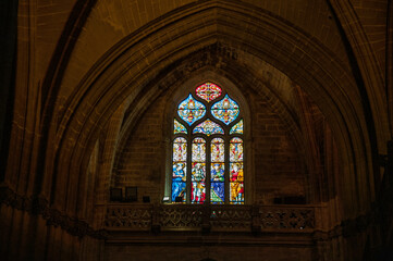 Obraz premium Interior of Seville Cathedral featuring illuminated stained glass window and gothic vaulted ceiling, Andalusia, Spain.