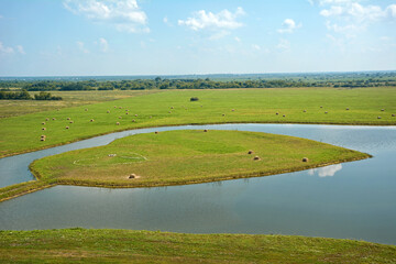 Large rolls of straw lie on a mowed field near a heart-shaped pond after harvest, autumn day in the field