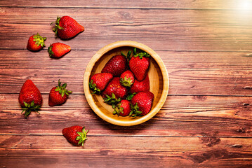 Fototapeta na wymiar Strawberries in a wooden bowl on wooden table. Top view with space for text and flare effect.