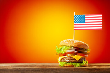 Close-up home made beef burger with american flag on the top on wooden table over orange background
