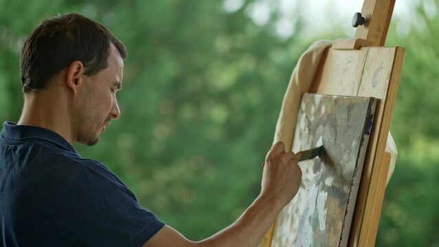 A male artist paints a picture in nature. A beautiful landscape, the artist paints an abstraction with a brush, inspired by trees and the sky. High quality 4k footage
